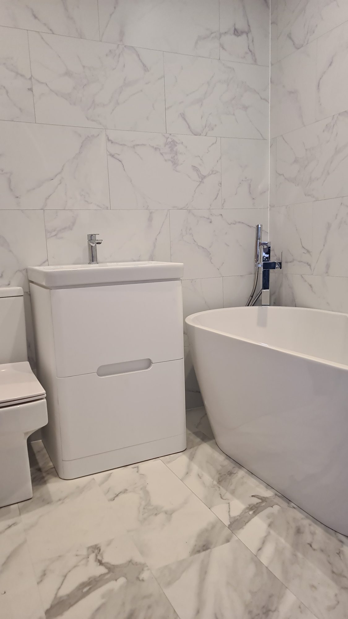 A white marble-look bathroom with a freestanding bath and a vanity unit