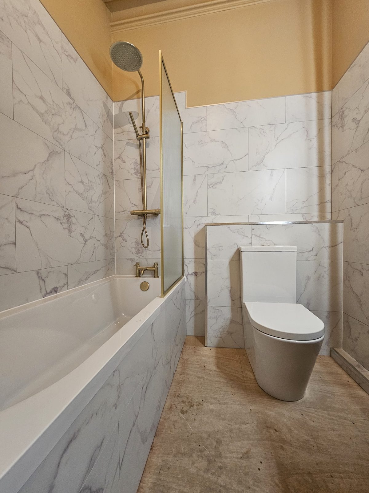 A bath with a brass-edged shower screen and marble-look tiles