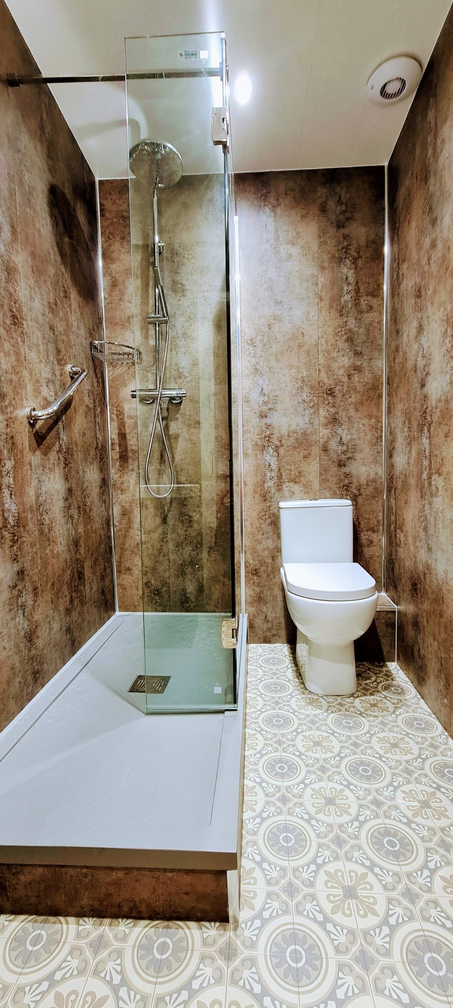 A shower with rust-effect wall panels, a glass screen and a patterned floor