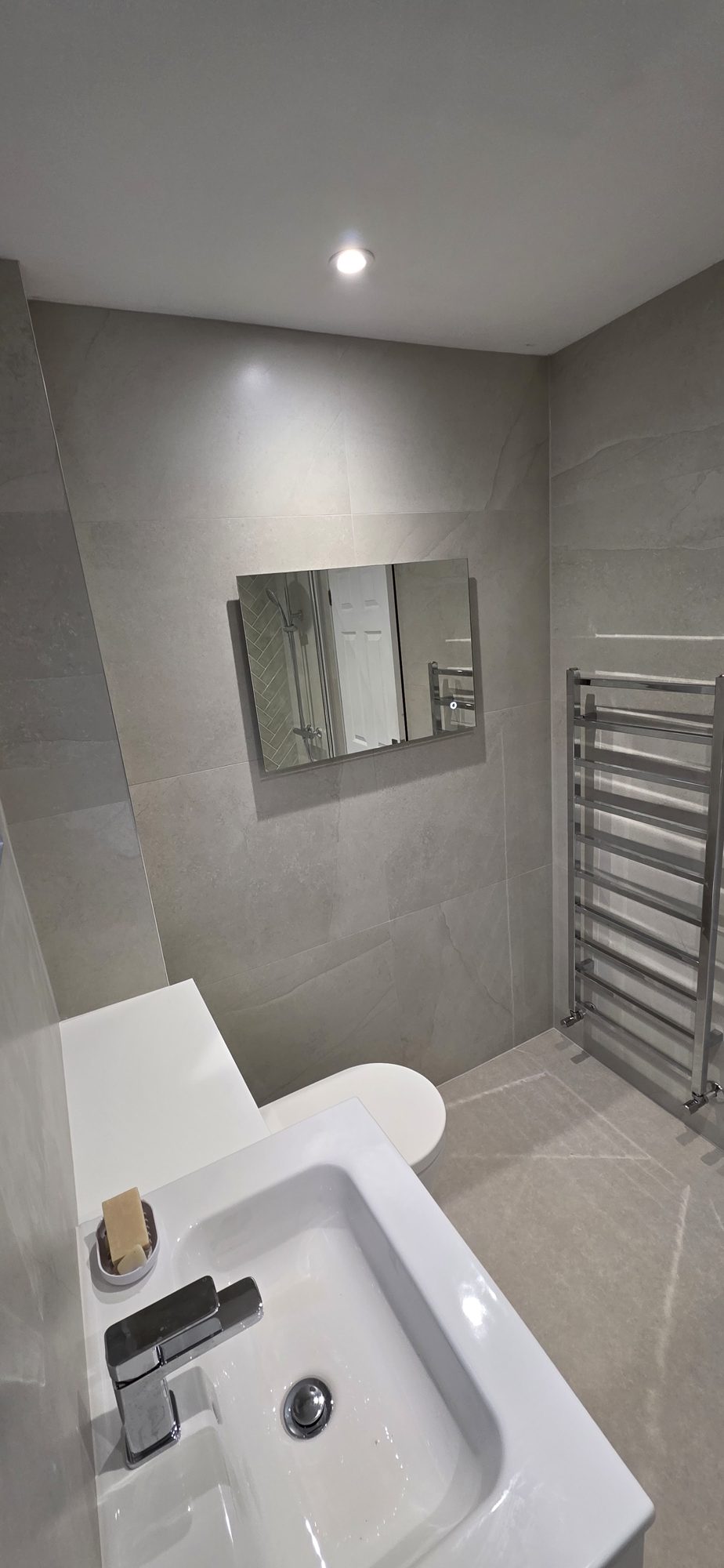 A grey tiled cloakroom with a basin and a chrome ladder radiator
