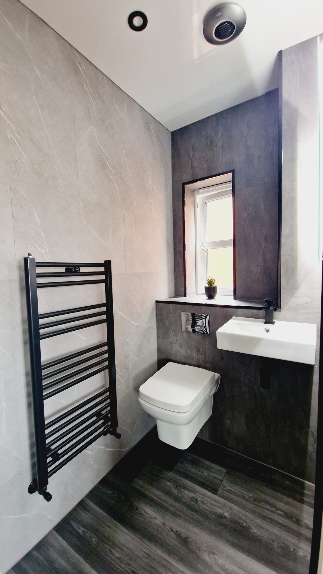 A wall-hung toilet beside a black ladder radiator on a dark feature wall