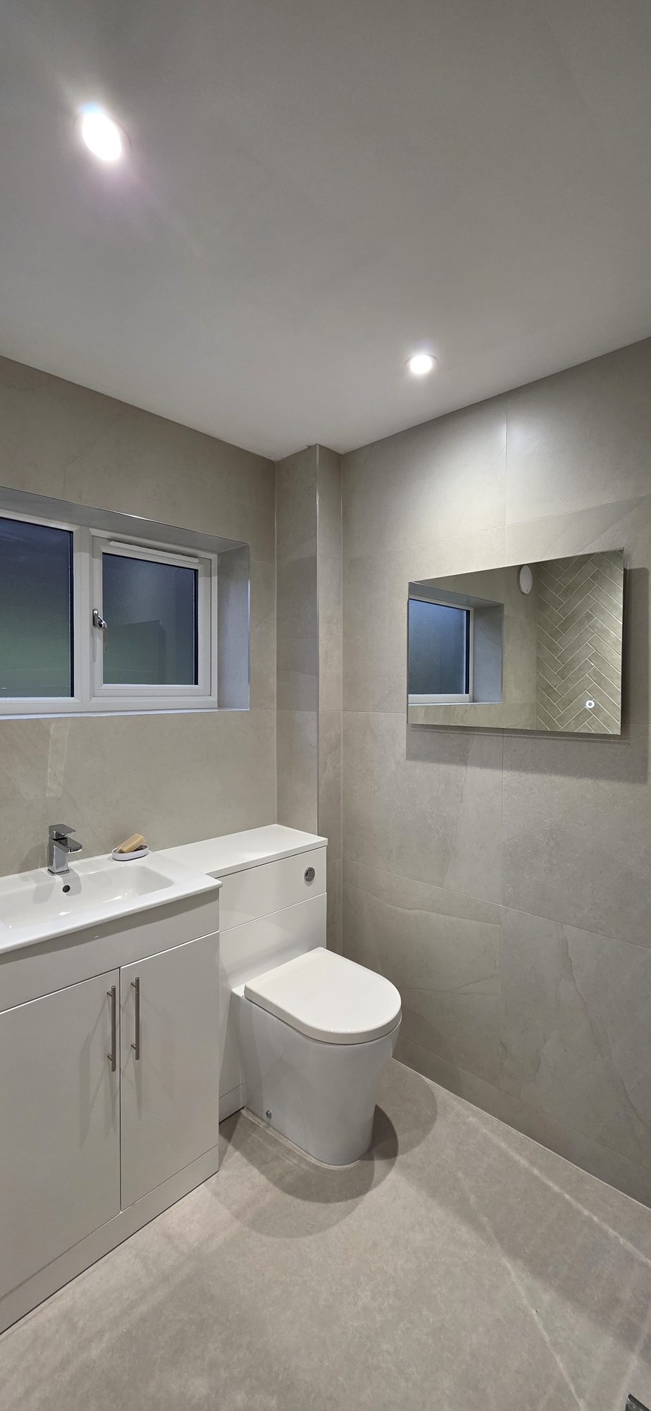 A grey tiled bathroom with a vanity unit and a back to wall toilet