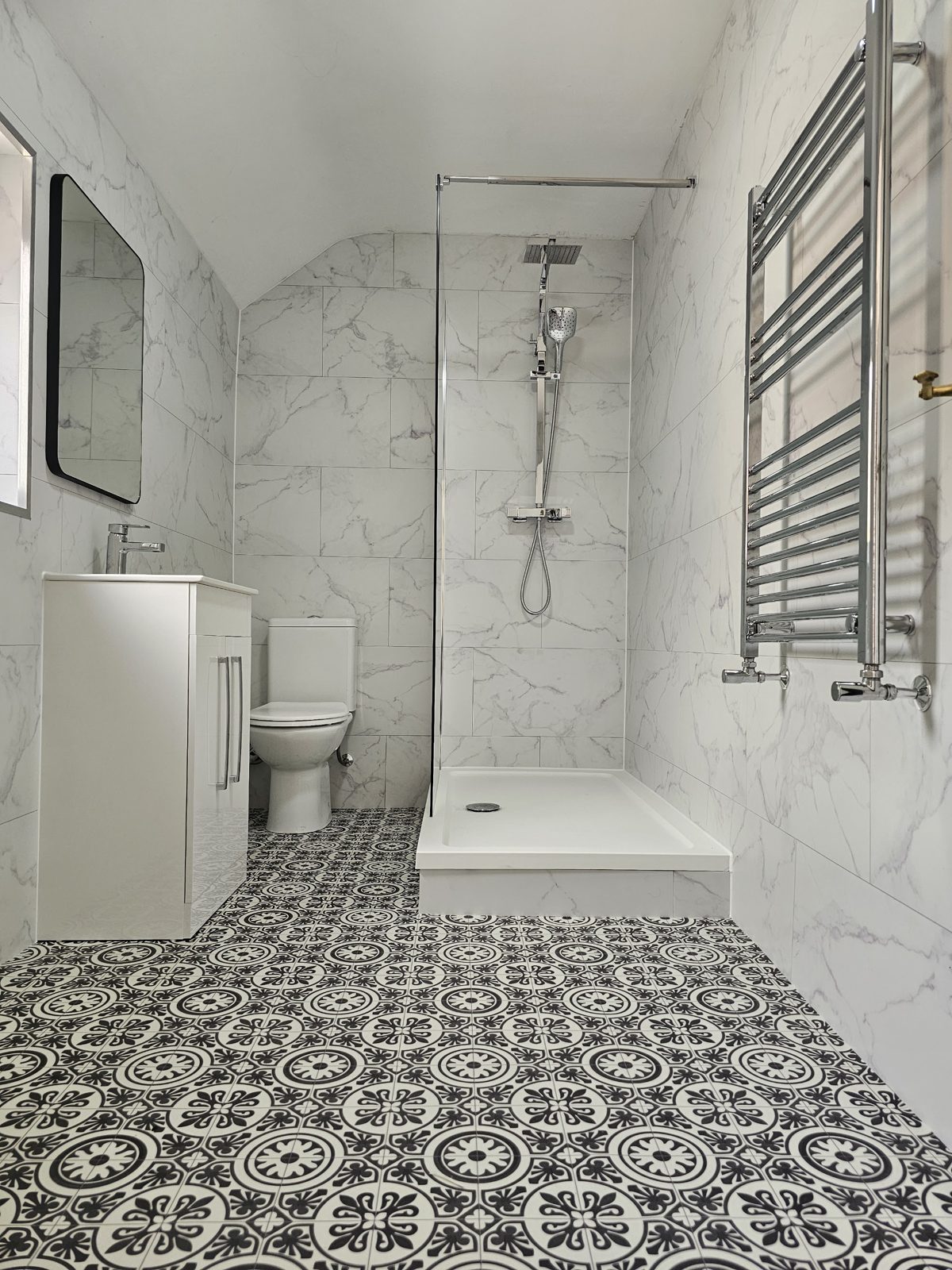 A marble-look shower with a chrome ladder radiator and a black and white patterned floor